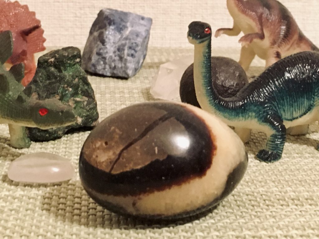 恐竜のフィギュアと卵のような石の画像